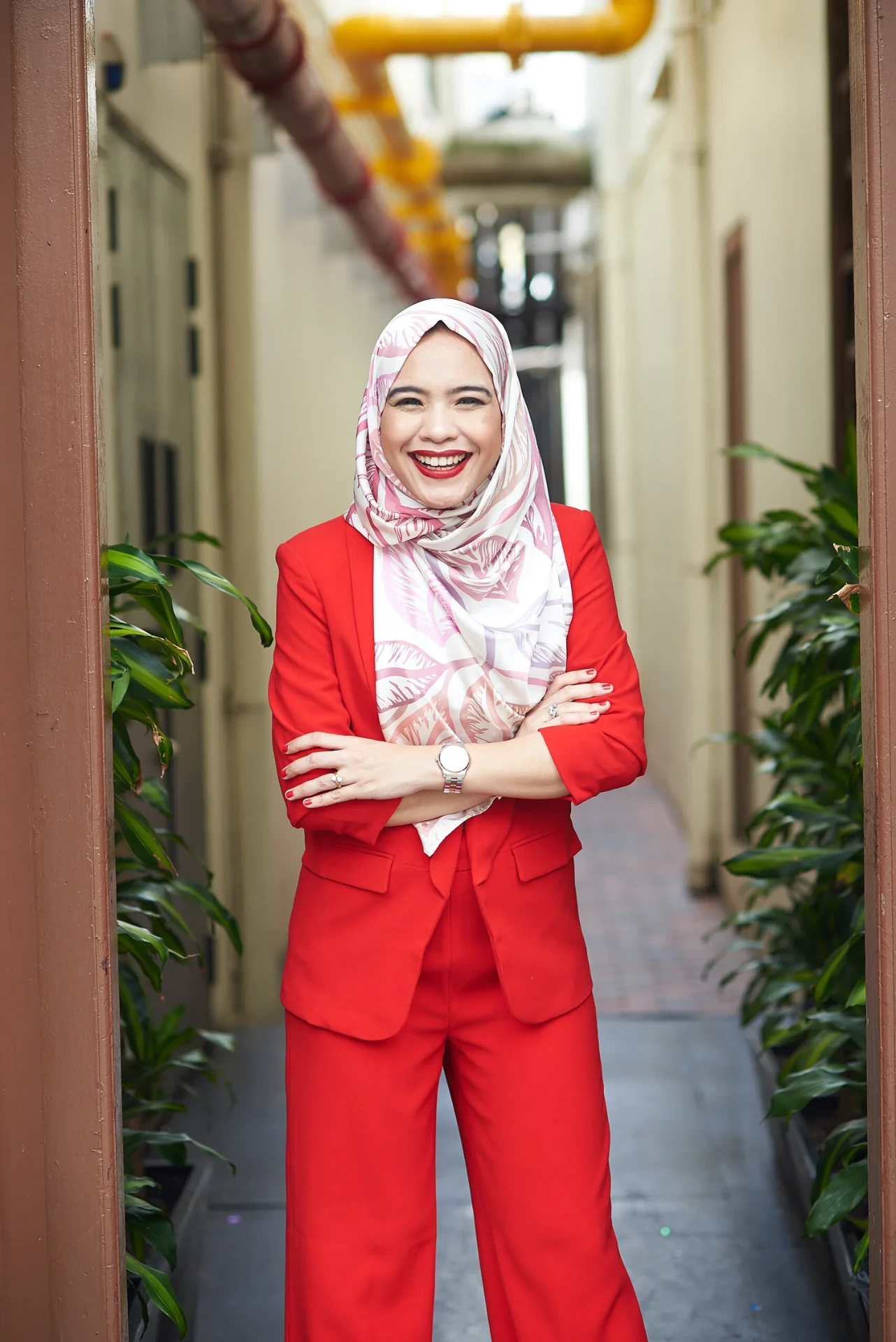 Bella Khaja smiling in a red suit, arms crossed, in a Singapore laneway